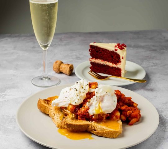 A glass of champagne beside poached eggs and red velvet cake